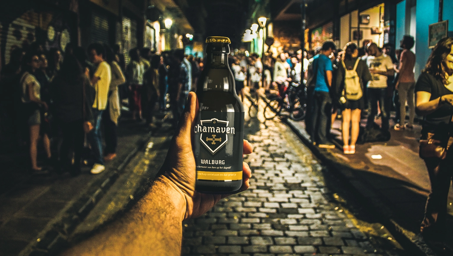 Hand die een Chamavan Walburg biertje vasthoudt met op de achtergrond een straat vol met mensen